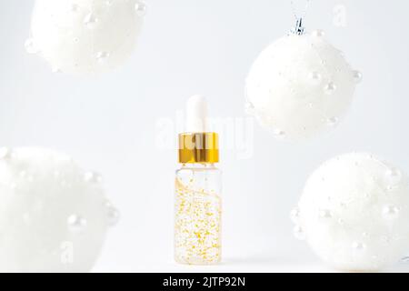 Flasche mit 24k Goldserum auf weißem Hintergrund mit weihnachtskugeln. Das Konzept der Hautpflege präsentiert sich für die Feiertage im neuen Jahr Stockfoto