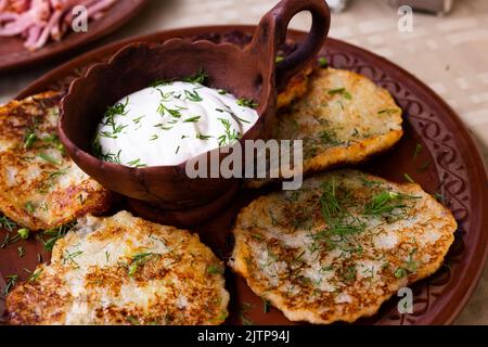 Kartoffelpfannkuchen mit Sauerrahm und Kräutern auf weißem Teller Stockfoto