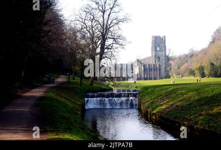 Menschen, die am Weir auf dem Fluss Skell auf dem Gelände der Fountains Abbey Zisterzienserkloster, North Yorkshire, England, Großbritannien, vorbeigehen. Stockfoto