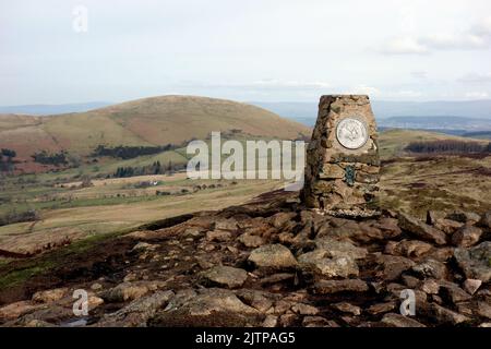 Die Trig-Säule auf dem Gipfel des Wainwright „Gowbarrow Fell“ mit „Little Mell Fell“ hinter dem Lake im Lake District National Park, Cumbria, Großbritannien. Stockfoto