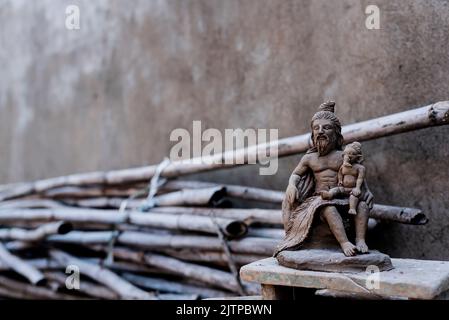 Kreative unvollendete Lehm Idol von herrn Ganesh sitzen auf den Schoß von herrn Shiva gehalten auf einer hölzernen Plattform mit Bambusstäben im Hintergrund Stockfoto