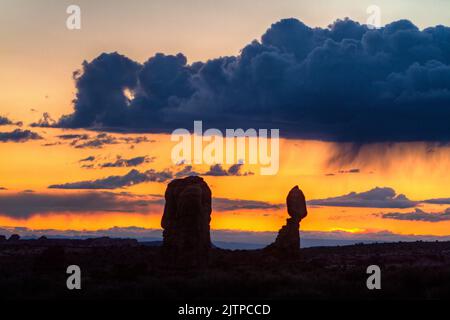 Sonnenuntergang Silhouette von Balanced Rock mit Virga von einem Regensturm über Arches National Park, Moab, Utah. Stockfoto