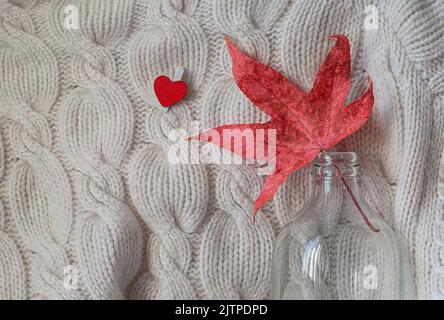 Kreative flache Lay-Komposition auf hellem Hintergrund. Rotes Blatt, Strickpullover und kleines Herz. Speicherplatz kopieren. Stockfoto
