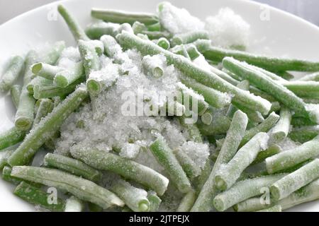 Gefrorene grüne Bohnen auf einem weißen Teller. Stockfoto