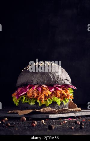 Pulled Schweinebauch Burger mit schwarzem Brot in einem dunklen Hintergrund Coleslaw und Salat mit Zwiebeln Stockfoto