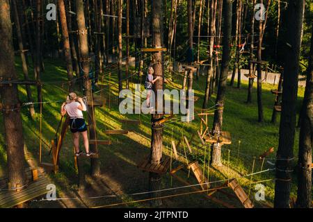 Eine Frau überwindet ein Hindernis in einer Seilstadt. Eine Frau in einem Waldseilpark. Stockfoto