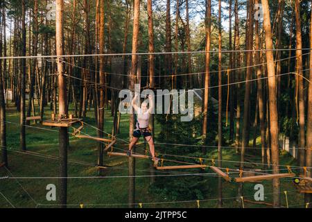 Eine Frau überwindet ein Hindernis in einer Seilstadt. Eine Frau in einem Waldseilpark. Stockfoto