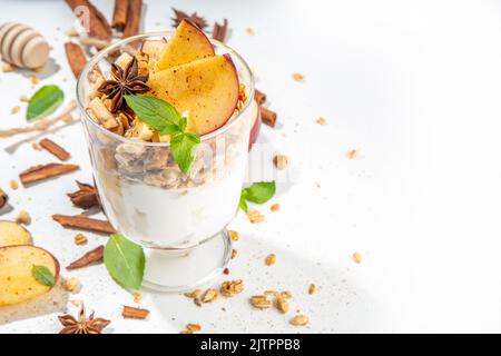 Apfelkuchen Müsli Käsekuchen, Frühstückssnack geschichtet Dessert mit Hafergranola, Frischkäse Joghurt, Honig, Apfelscheiben und Zimt Gewürze auf weiß Stockfoto