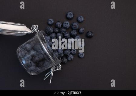 Frische Heidelbeeren im Glasglas isoliert auf schwarzem Hintergrund, rohe Beeren in der Küche, Kosmetik und Medizin verwendet, Nahaufnahme Stockfoto