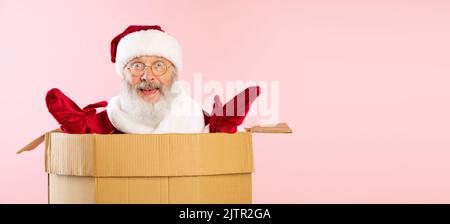 Porträt eines fröhlichen älteren Mannes, Weihnachtsmann, der in einem Karton sitzt. Frohe Feiertage Stockfoto