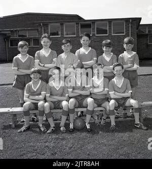 1965, historische, Junior-Schule Fußball-Mannschaftsgruppe Foto. Fröhliche junge Jungen, die das Trikot und die Stiefel der Ära tragen; Hemden mit V-Ausschnitt, Shorts mit Zugband und Fußballschuhe, viele mit lederbezogenen Stahlköpfen, einige mit hohem Knöchel. Seveal der Jungen trägt den beliebten „Gola“-Stiefel des Tages, einen Lederfußballschuh mit einem niedrigeren Schnitt unter dem Knöchel, der von Botterill's aus Bozeat aus Northamptonshire, England, hergestellt wurde, einem 1895 gegründeten Schuhunternehmen. Im Jahr 1960s trugen die Spieler des berühmten FC Liverpool Gola Fußballschuhe. Stockfoto