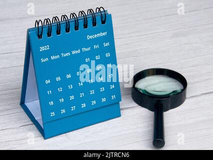 Dezember 2022 blauer Tischkalender auf Holzschreibtisch mit Kopierraum und Lupe. Stockfoto