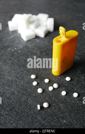 Vergleich von künstlichem Süßstoff und Zuckerwürfelbehälter auf Schwarz Stockfoto