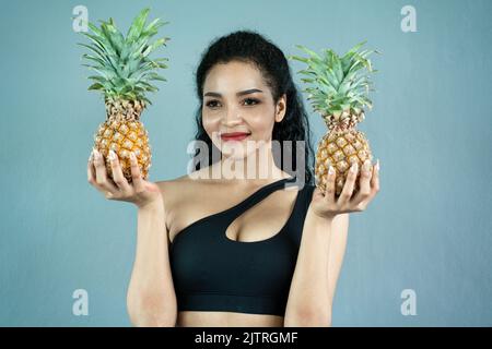 Glückliche junge Frau, die Ananas zeigt. Ananasfrucht Frau lächelt gesund und fröhlich. Gemischtes asiatisches/kaukasisches Modell mit Ananas Stockfoto