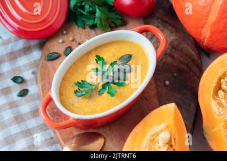 Kürbissuppe in einem Topf mit Petersilie und Kürbiskernen auf Schneidebrett. Herbstfutter, Draufsicht. Stockfoto