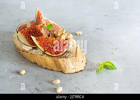 Knusprige Bruschetta (Toast) mit weichem Ricotta, reifen Feigen, Walnüssen und Pinienkernen, Minze und Honig auf hellem Hintergrund. Stockfoto