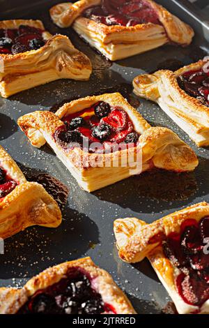 Blätterteig mit Beeren (herb) auf einem Backblech, portioniertes Sommerdessert bei hartem Licht. Stockfoto