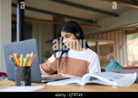 Biracial Teenager Mädchen trägt Kopfhörer und studieren über Laptop auf dem Schreibtisch zu Hause Stockfoto