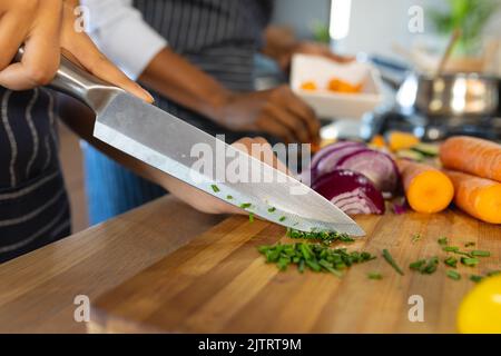 Mittelteil der Biracial Tochter und Mutter schneiden frisches Gemüse auf Schneidebrett in der Küche Stockfoto