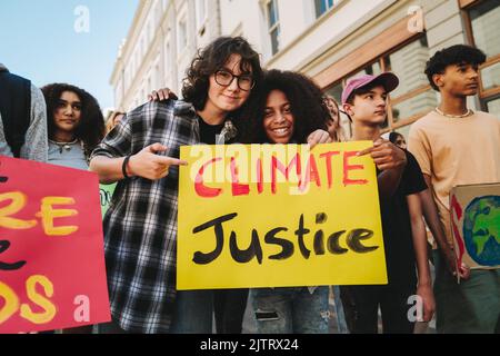 Glückliche Teenager-Mädchen halten ein Plakat bei einem März zum Klimawandel. Gruppe multikultureller Jugendaktivisten, die gegen die globale Erwärmung protestieren. Vielfältig Stockfoto