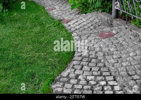 Fußgängerweg aus grauen Granit Pflastersteinen in einem Park mit grünem Gras in der Nähe eines Fußgänger gepflasterten Weg für Spaziergänge im Garten, Nahaufnahme Landschaft Stockfoto