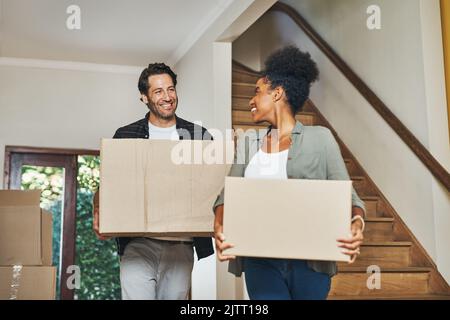Paar Hausbesitzer, die einziehen, Kisten tragen und in einem neu erworbenen Haus als Immobilieninvestoren auspacken. Lächelnder, fröhlicher und fröhlicher interrassischer Mann Stockfoto