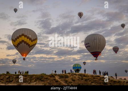 GOREME/TÜRKEI - 30. Juni 2022: Touristen beobachten die Heißluftballonshow über goreme bei Sonnenaufgang Stockfoto