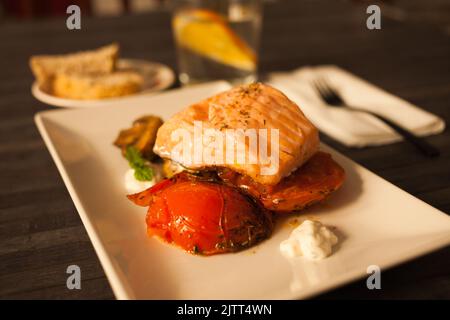 Gedünstetes Meerforellenfilet auf gebratenen Pilzen mit Tomaten auf einem weißen Teller serviert Stockfoto