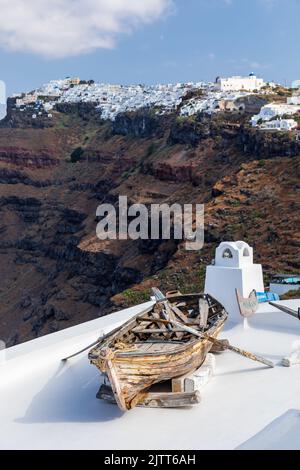 Altes verwittertes Ruderboot aus Holz auf einem Dach in Firostefani mit Imerovigil im Hintergrund, Santorini, Kykladen-Inseln, Griechenland, Europa Stockfoto