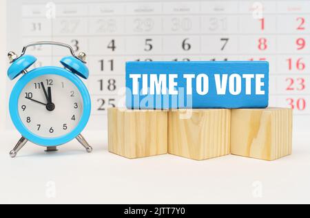 Zeitkonzept. Vor dem Hintergrund des Kalenders ist ein Wecker, Würfel und ein blauer Block mit der Aufschrift - Time to Vote Stockfoto