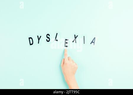 Kinderhand, die das Wort Dyslexie aus Buchstaben auf hellblauem Hintergrund baut. Dyslexie Bewusstsein, helfen Kindern mit Lesen, Lernschwierigkeiten Stockfoto