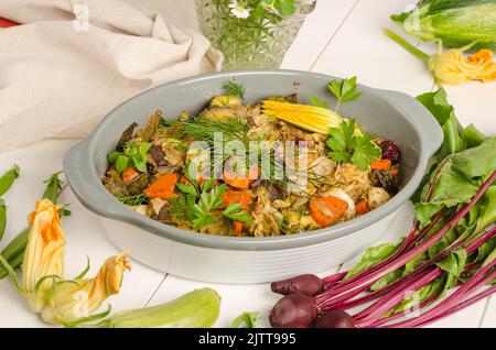 Im Ofen gebackenes Gemüse mit Gewürzen und Kräutern in einer Auflaufform auf weißem Holzhintergrund. Stockfoto