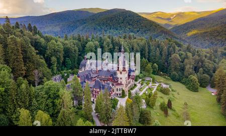 Luftaufnahmen von Schloss Peles in Rumänien. Die Fotografie wurde von einer Drohne bei Sonnenuntergang in einer höheren Höhe mit Bergen im Hintergrund aufgenommen. Stockfoto