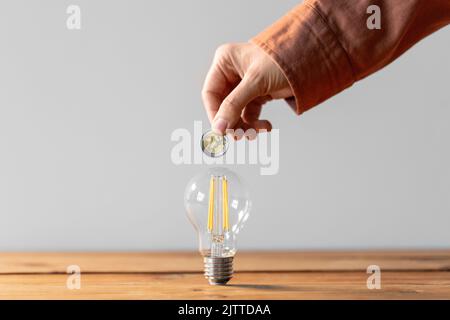 Nahaufnahme der Hand mit Münze und Glühbirne auf dem Tisch Stockfoto