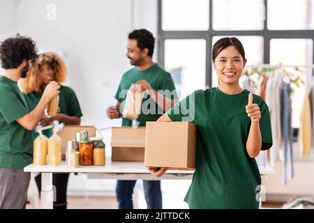 Weibliche Freiwillige mit Essen in der Box zeigt Daumen nach oben Stockfoto