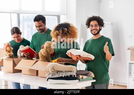 Freiwillige packen Sachen und zeigen Daumen hoch Stockfoto