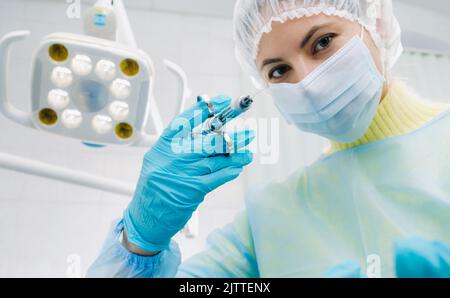 Ein maskierter Zahnarzt hält eine Injektionsspritze für einen Patienten im Büro. Stockfoto