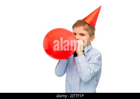 Kleiner Junge in Geburtstagsfeier Hut weht Ballon Stockfoto