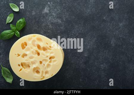 Käse Maasdam oder Radamer. Stück Käse auf schwarzem Marmor oder Stein Standa auf schwarzem Beton Hintergrund. Draufsicht. Freier Speicherplatz für Ihren Text. Stockfoto