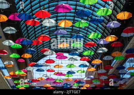 In einem großen Zimmer hängen viele bunte Regenschirme hoch von der Decke. Stockfoto