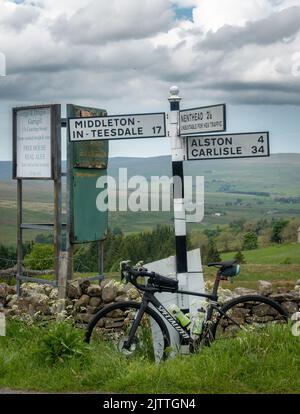 Traditionelle Wegweiser in der Nähe von Garrigill mit einem Rennrad, das sich gegen den Pfosten auflehnt und Middleton-in-Teesdale, Alston, Carlisle und Nent beschildert Stockfoto