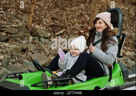 Mutter und Tochter fahren auf Schienen mit einem elektrischen Schlitten. Stockfoto