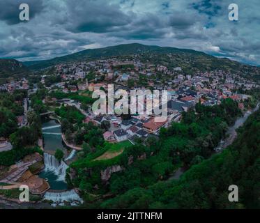 Wasserfall am Pliva-Fluss und Panorama der Stadt Jajce im Westen Bosniens. Drohnenperspektive oder Luftaufnahme von Jajce an einem bewölkten Tag. Stockfoto