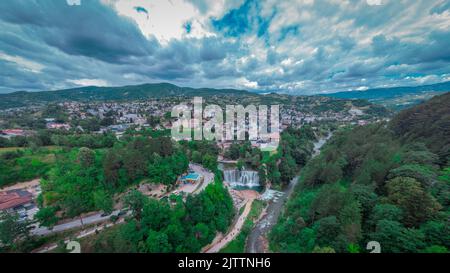 Wasserfall am Pliva-Fluss und Panorama der Stadt Jajce im Westen Bosniens. Drohnenperspektive oder Luftaufnahme von Jajce an einem bewölkten Tag. Stockfoto