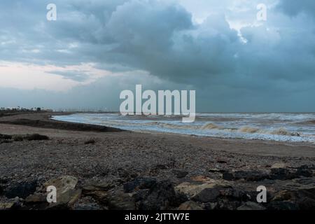 Blick auf den Strand von Sagunto mit dem rauen Meer mit großen Wellen nach dem Sturm unter einem dramatischen Himmel. Puerto de Sagunto - Valencia Stockfoto