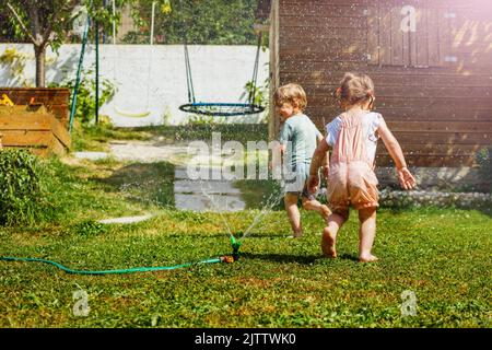 Zwei Kinder haben Spaß im Garten - spielen mit Wasser auf dem Rasen Stockfoto