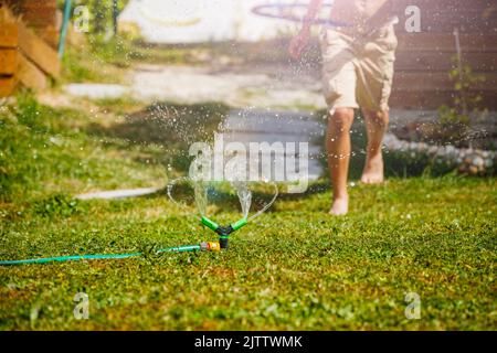 Beine eines Kindes, das auf dem Rasen um den Wasserregner herumläuft Stockfoto
