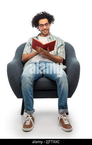 Glücklicher lächelnder Mann beim Lesen des Buches, der auf einem Stuhl sitzt Stockfoto