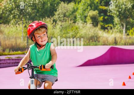 Nahaufnahme eines kleinen lächelnden Jungen, der auf einem kleinen Fahrrad fährt Stockfoto