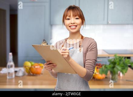 Frau in Schürze mit Klemmbrett und Stift in der Küche Stockfoto